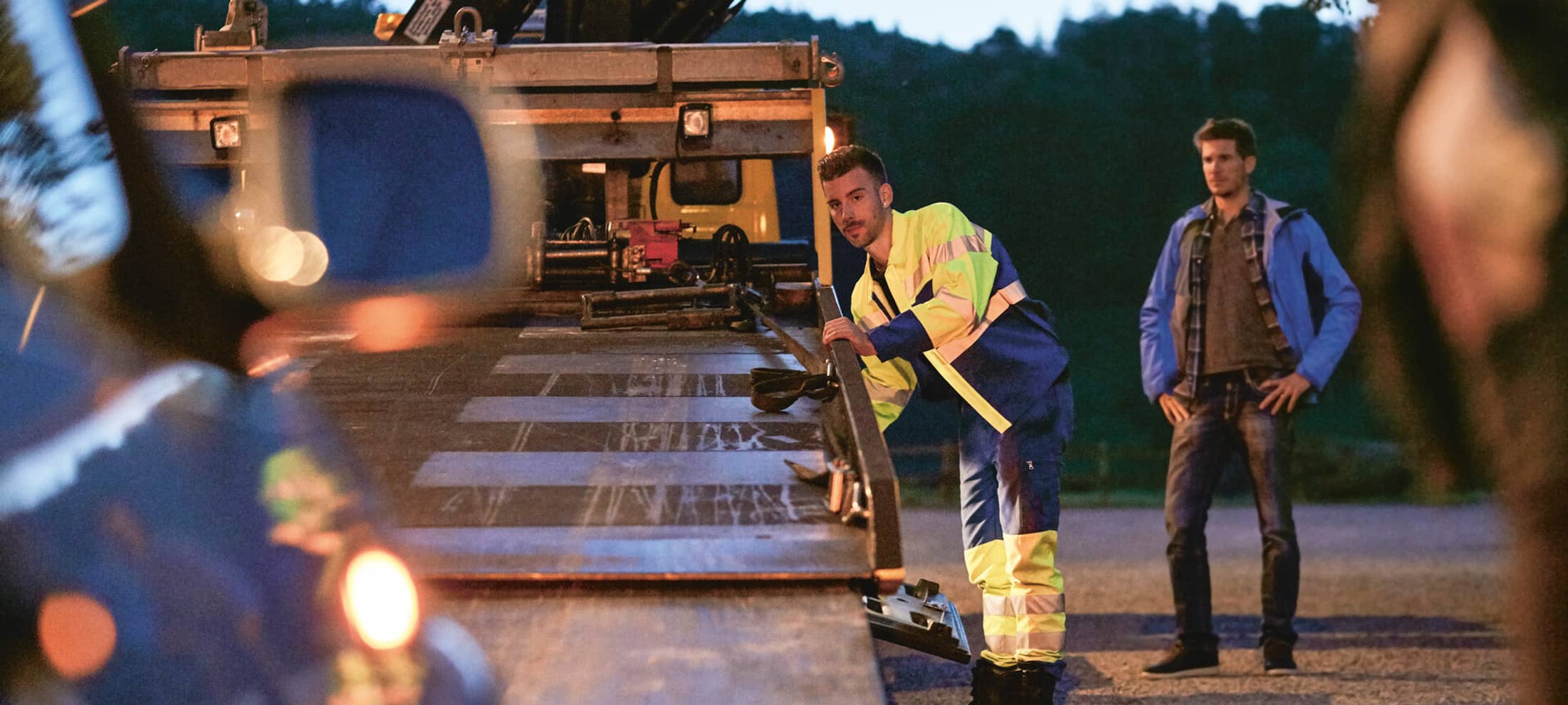 Un préposé au remorquage charge un véhicule apparemment en panne. Le détenteur du véhicule se tient à côté de lui et regarde. 