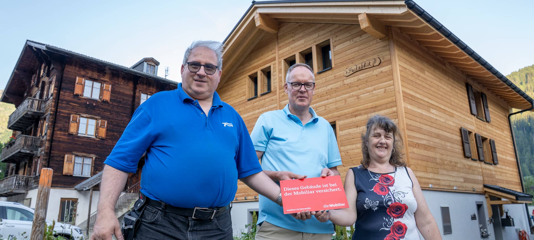 Vor einem Holzhausneubau stehen drei Personen.