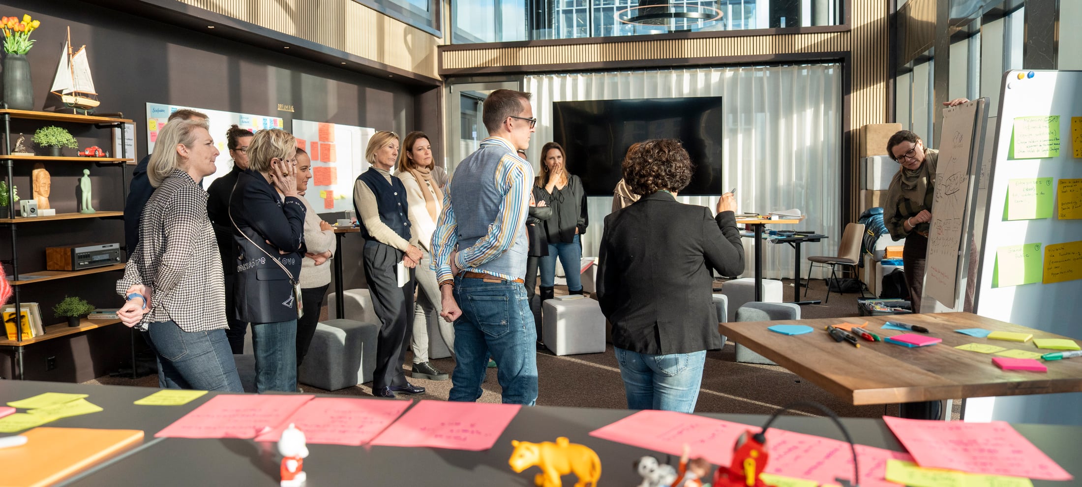 Eine Workshopgruppe steht im Raum und bespricht gemeinsam ihre Ideen. Im Vordergrund liegen Post-its.