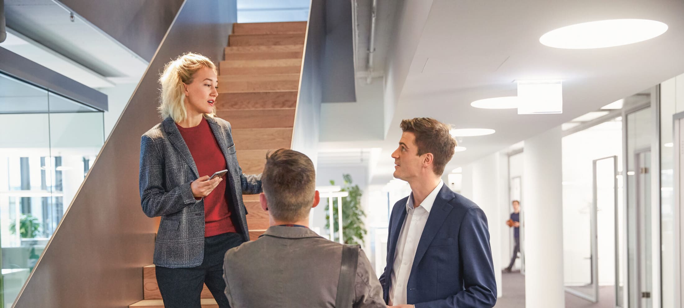 Assicurazione PMI: una donna su una scala di un ufficio moderno parla con due colleghi vestiti in modo formale.