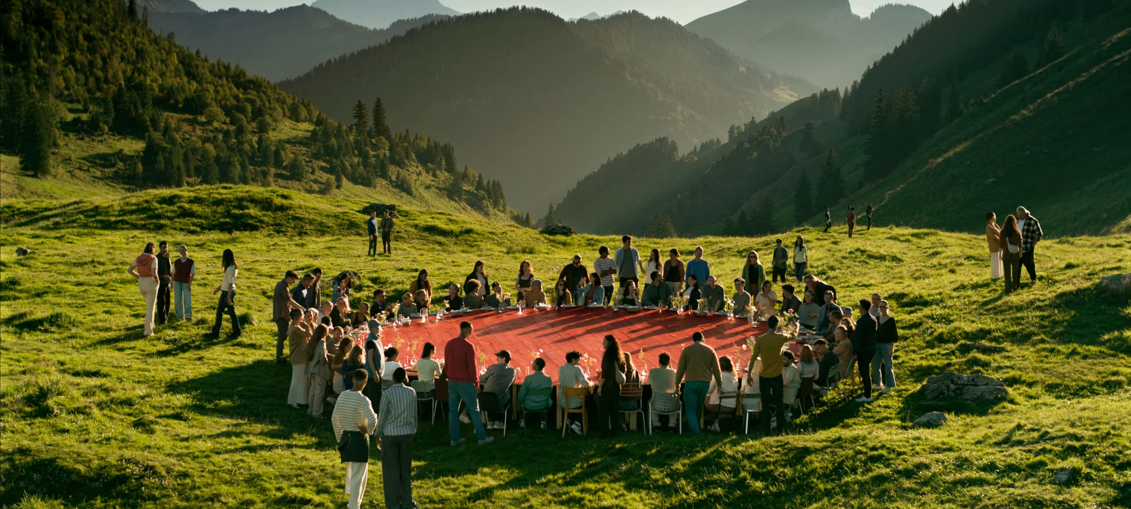 Eine Gruppe von Leuten sitzen an einem grossen roten runden Tisch auf einer grünen Wiese