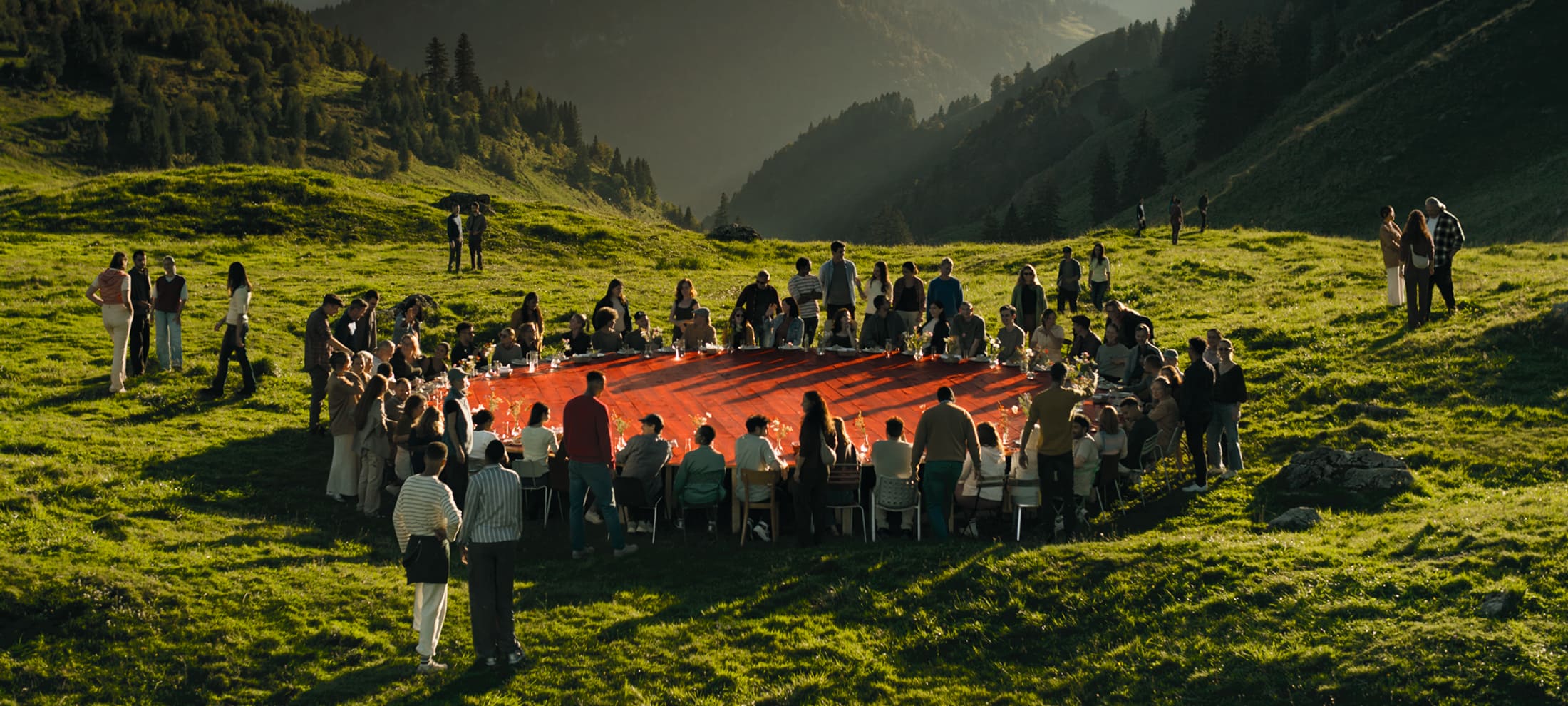 Une grande table rouge dans la nature autour de laquelle de nombreuses personnes sont assis.
