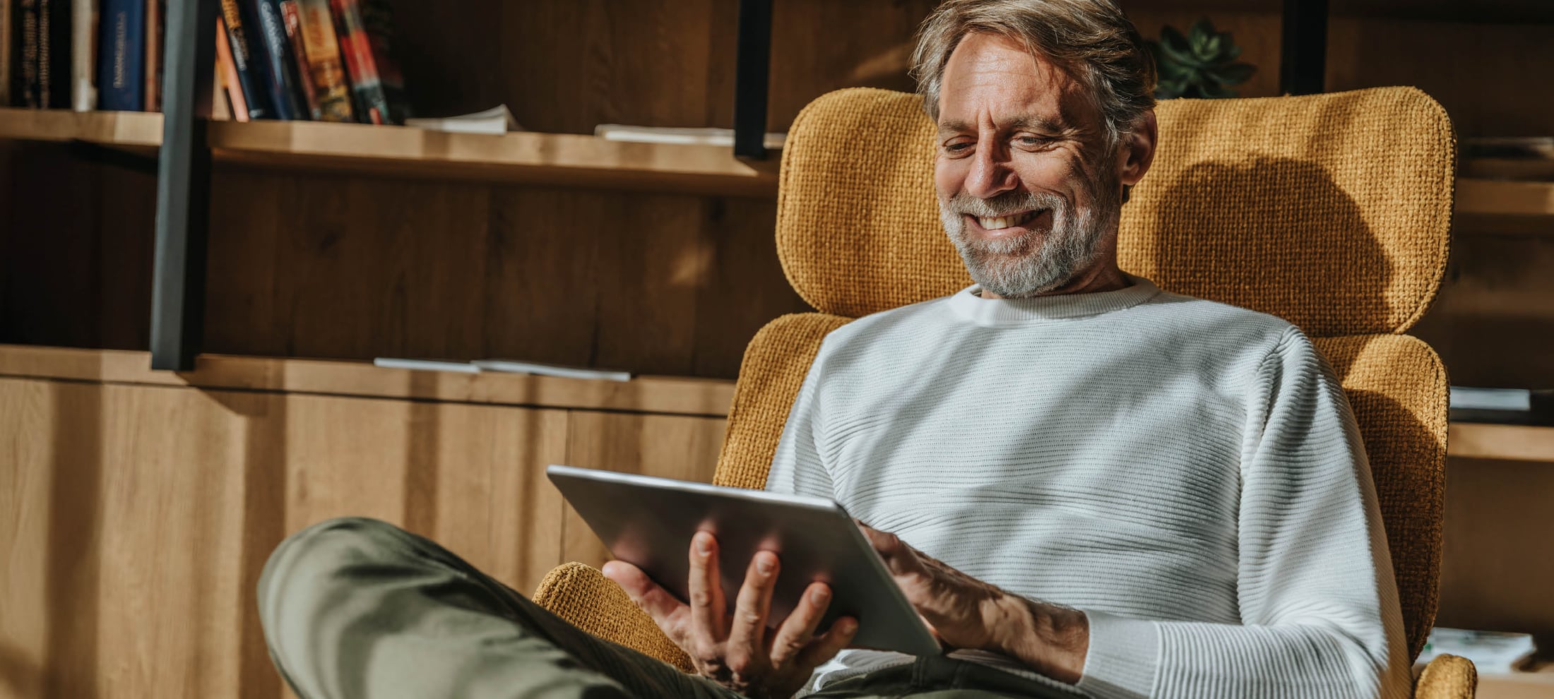 ein ältere Mann sitzt mit dem iPad in einem Sessel