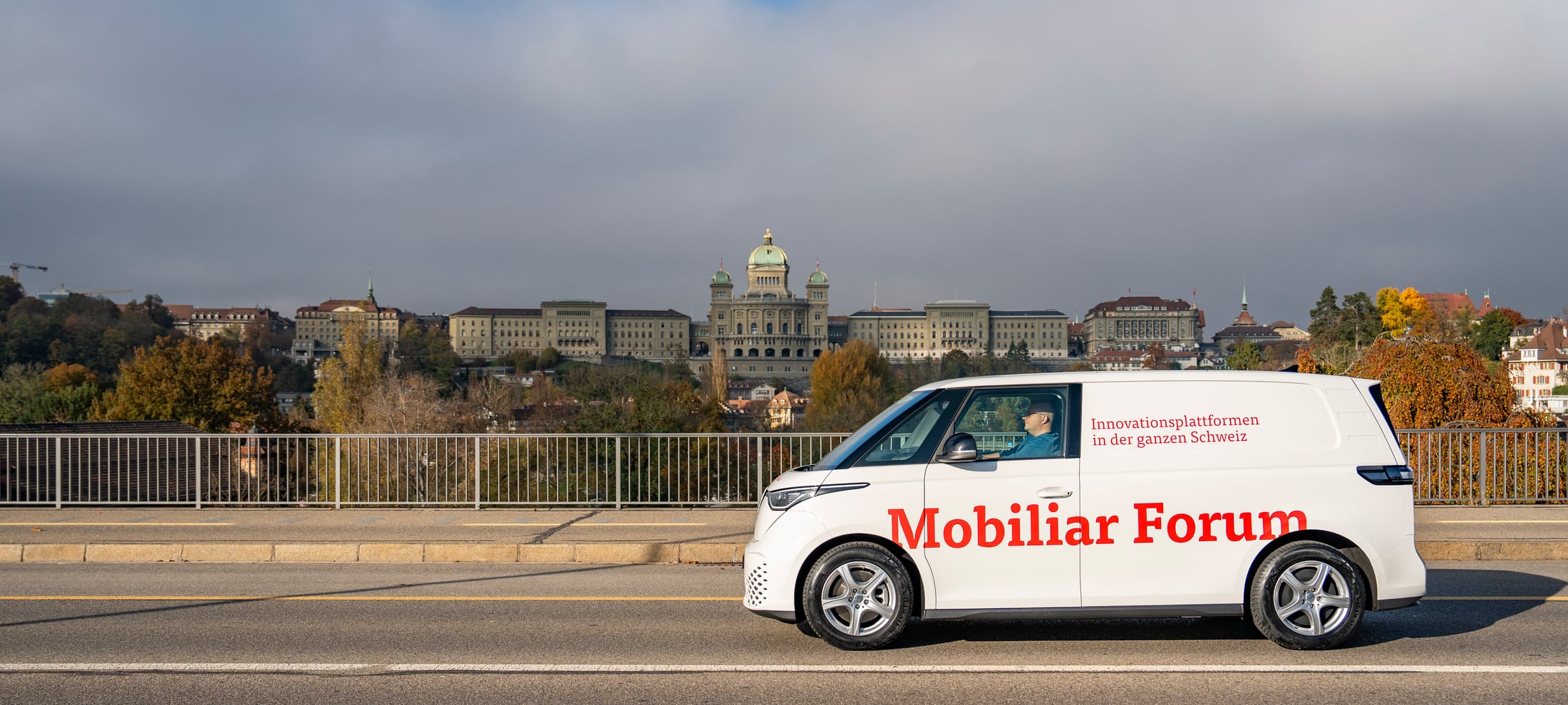 Ein weisser VW-Bus ist mit Mobiliar Forum angeschrieben und fährt über die Monbijoubrücke. Im Hintergrund sieht man das Bundeshaus.