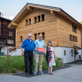Vor einem Holzhausneubau stehen drei Personen.