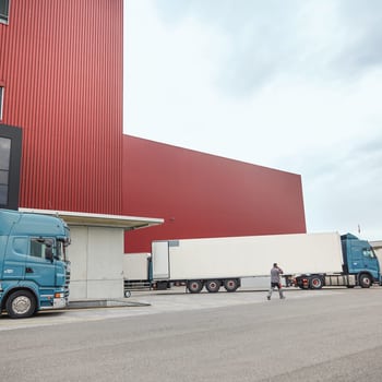 Es sind drei LKW zu sehen, ein Mann läuft zügig zum hinteren LKW im Bild und telefoniert am Handy.