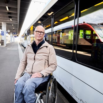 Un homme en fauteuil roulant se trouve au quai d’une gare devant un train à l’arrêt. 