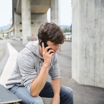 Junger Mann ist am Telefon und sitzt mit Skateboard auf einer Treppe.