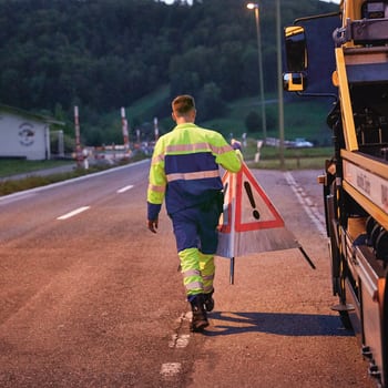 Ein Mann vom Pannendienst stellt ein Warnschild auf, das auf einen Unfall hinweist.