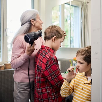 Des enfants se brossent les dents sous la surveillance de leur grand-maman dans la salle de bain de leur nouvel appartement. 
