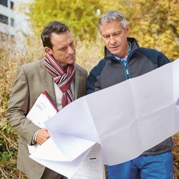Zwei Männer sehen sich gemeinsam einen Bauplan an. 