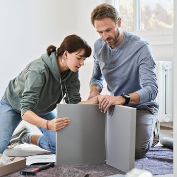 Un homme aide une jeune femme à monter un nouveau meuble. 
