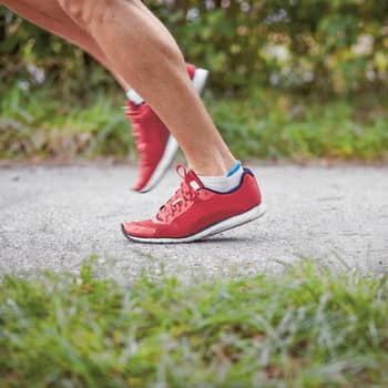 Une personne court sur une route goudronnée avec de l’herbe à gauche et à droite avec des baskets rouges. Sur la photo, on ne voit que ses pieds. 