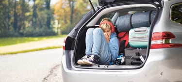 Un garçon est assis dans le coffre ouvert chargé de ses bagages.