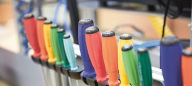 Schraubenzieher verschiedener Grössen mit unterschiedlich farbigen Griffen stecken ordentlich aufgereiht in einer Halterung in einer Werkstatt. 