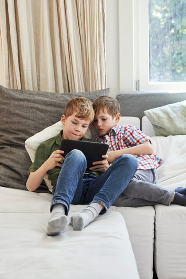 Deux enfants jouant avec une tablette sur le sofa familial 