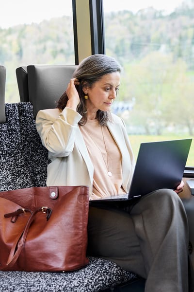 Una donna seduta in treno con un laptop aperto in ginocchio.