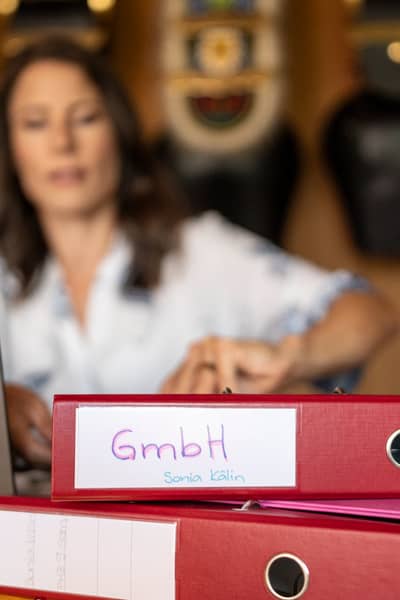 Sonia Kälin sitzt an ihrem Arbeitstisch und blickt auf ihre Unterlagen. Im Vordergrund ein Ordner, der mit GmbH angeschriebe ist.