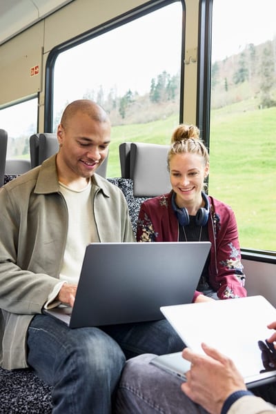 Eine Gruppe junger Menschen sitzt im Zug, alle arbeiten an einem Laptop oder Tablet. 