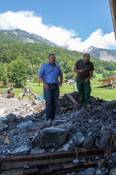 Versicherungsberater und Kunde stehen auf einem Geröllhaufen vor dem Haus, nach dem Unwetter in Brienz