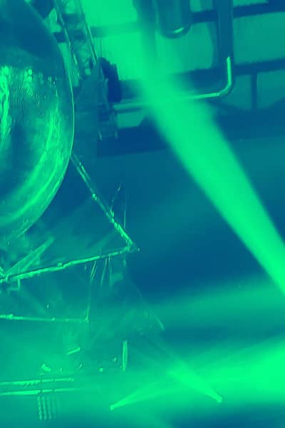 Boule de disco au plafond d’un club, est éclairé par des phares, l’image a un ton vert-bleu.