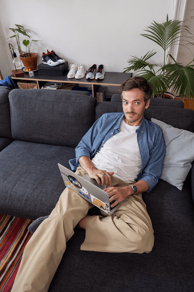 Junger Mann liegt auf der Couch und schaut in sein Notebook.