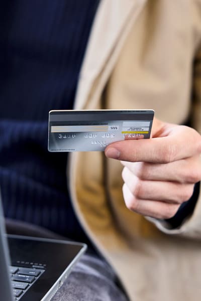 Nahaufnahme von einer Person, die eine Kreditkarte in der Hand hält, um in einem Onlineshop etwas zu kaufen. 