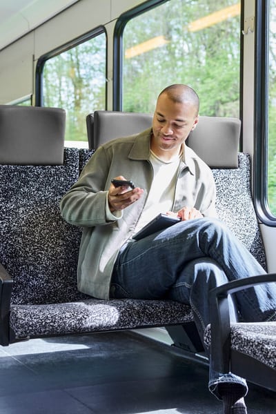 Junger Mann sitzt im Zug und schaut auf sein Smartphone 