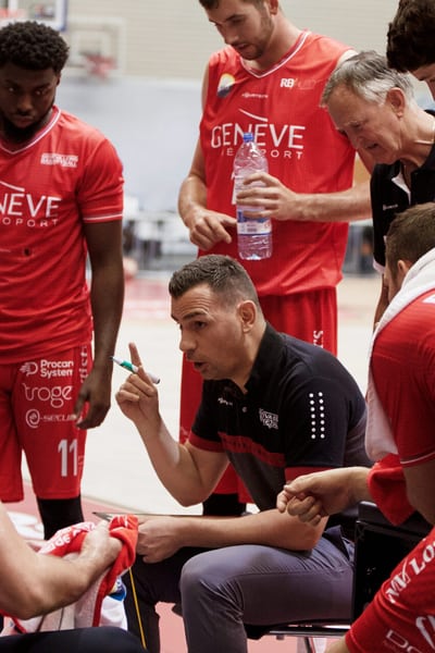 Une équipe de basket-ball en maillot rouge sponsorisé par la Mobilière discute au bord du terrain