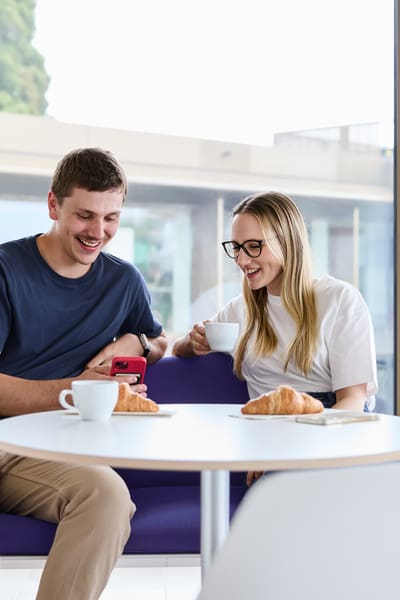 Zwei junge Mitarbeitende zeigen sich in der Kaffeepause etwas auf dem Handy