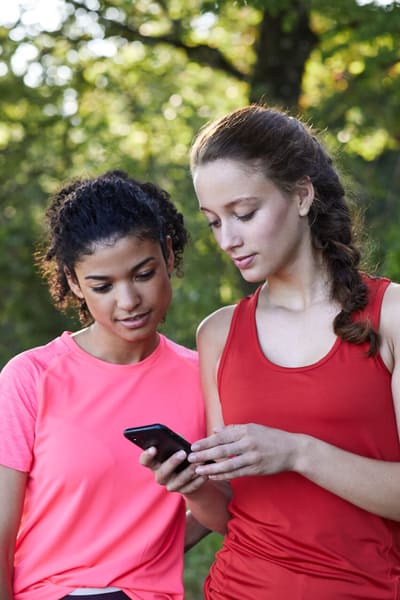 Zwei Frauen schauen beim Joggen auf ein Handy.