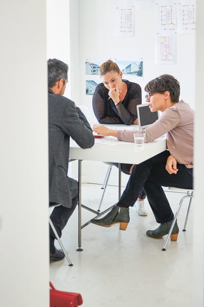 Blick in ein Büro. An einem Tisch sitzen drei Personen und besprechen etwas.