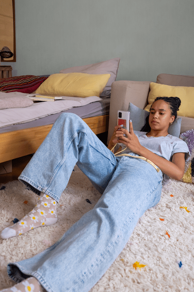 Junge Frau liegt auf dem Teppich in ihrem Zimmer und scrollt am Smartphone durch Social Media