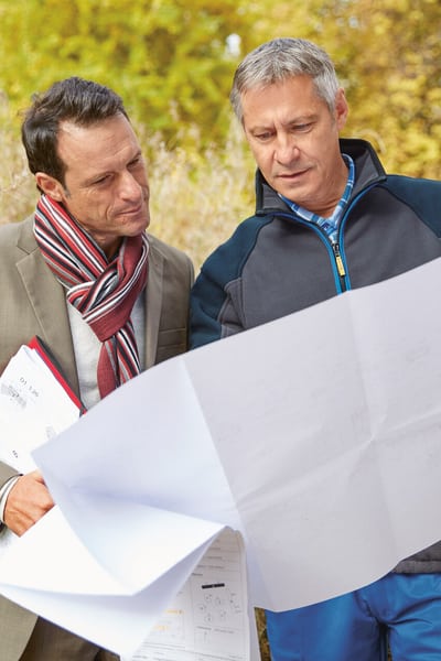 Deux hommes se tiennent devant une colonie et regardent un plan de construction.