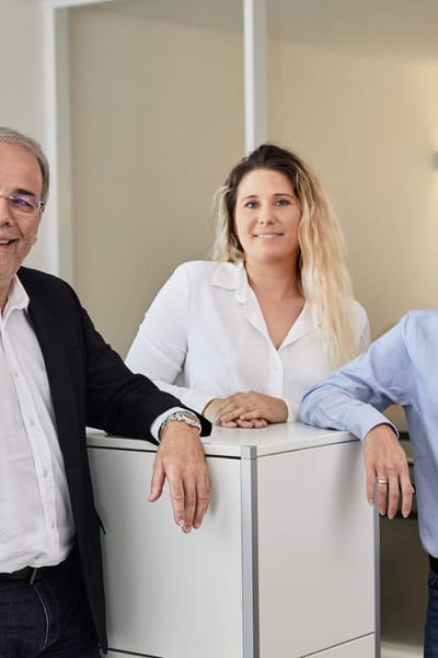 Due uomini e una donna sono in piedi uno accanto all’altro nell’ufficio e guardano la telecamera