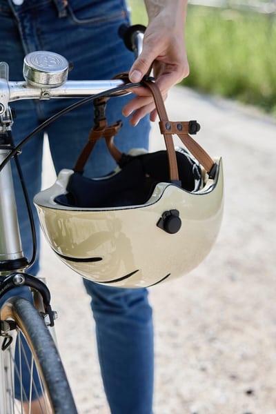 Eine Person schiebt ein Velo und hat einen beigen Velohelm in der Hand. Sichtbar ist nur der Ausschnitt mit dem Lenker. 