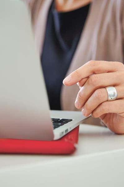 Eine Frau arbeitet am Laptop. Sichtbar sind nur ihre linke Hand und Oberkörper.