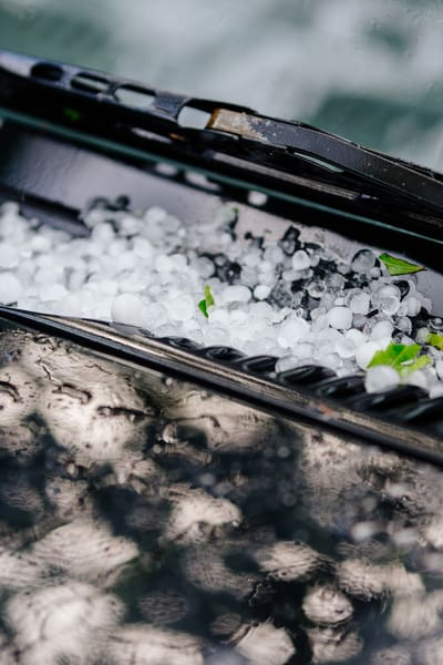Si vede solo una piccola parte del cofano e del parabrezza con i tergicristalli, lo spazio tra di loro è pieno di chicchi di grandine. 