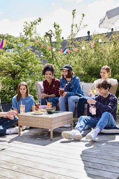 Un groupe de jeunes est assis sur une terrasse et à côté d’un lounge, buvant des verres et riant ensemble. 