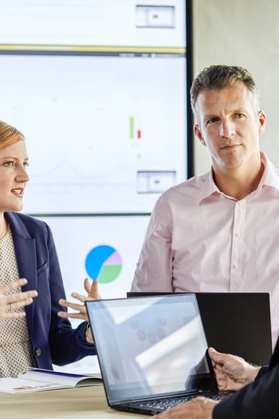 3 persone discutono davanti al muro con molti schermi