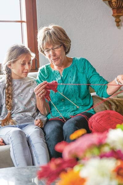 Une femme âgée montre à sa petite-fille comment tricoter sur le canapé dans le salon.