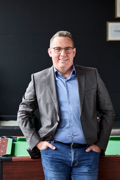 Ein Mann steht vor einem Billardtisch und blickt direkt in die Kamera.