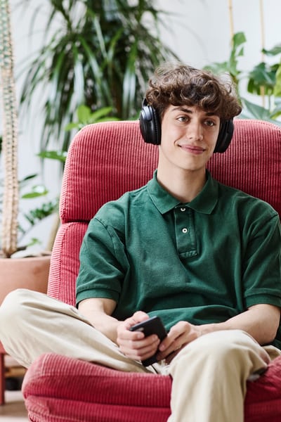 Un giovane uomo, seduto in poltrona, ascolta la musica con le cuffie. 