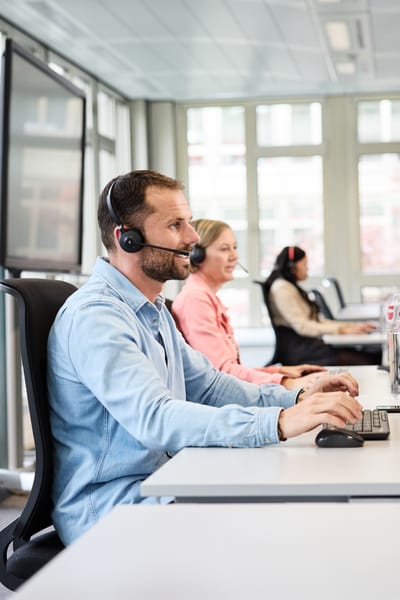 Mitarbeiter mit Headset während eines Calls am Computer arbeitend 