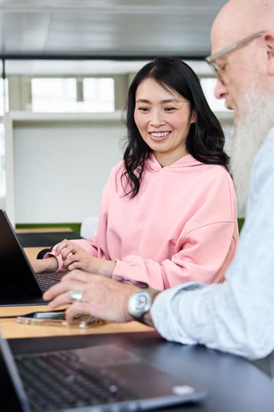 Jüngere und älterer Mitarbeiter im Gespräch vor dem Laptop