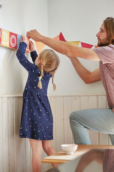 Ein Vater der mit seiner kleinen Tochter farbige Wimpel an der Wand anbringt.