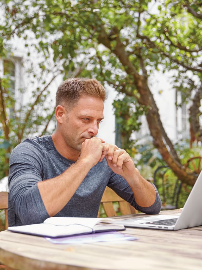 Ein Mann sitzt im Garten, vor ihm ein aufgeklappter Laptop, und recherchiert zum Thema Änderungskündigung Schweiz. 