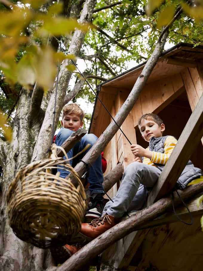 Zwei Kinder sitzen in einem Baumhaus aus Holz und spielen mit einem Seil. Sinnbild für den Ratgeber zu Licht und Schatten.