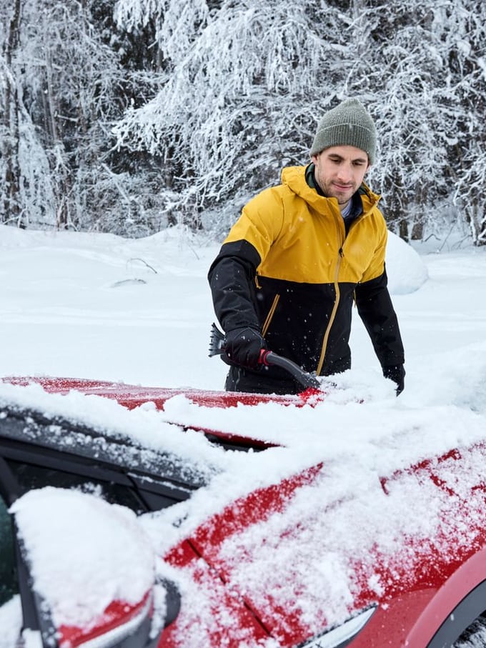 Jeune homme grattant les vitres de sa voiture en hiver