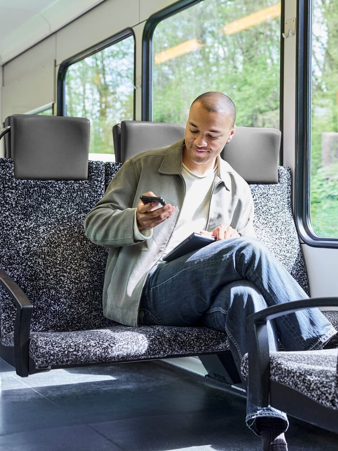 Junger Mann im Zug, hält sein Smartphone in der Hand. Er ist zufrieden.